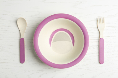 Photo of Colorful bowl with fork and spoon on white wooden table, flat lay. Serving baby food