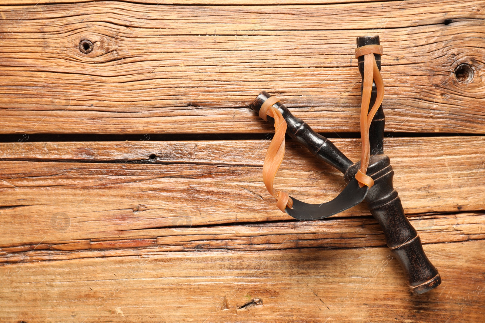 Photo of Black slingshot with leather pouch on wooden table, top view. Space for text