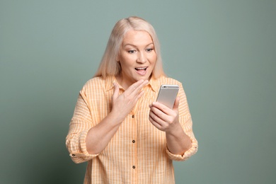 Mature woman using mobile phone on color background