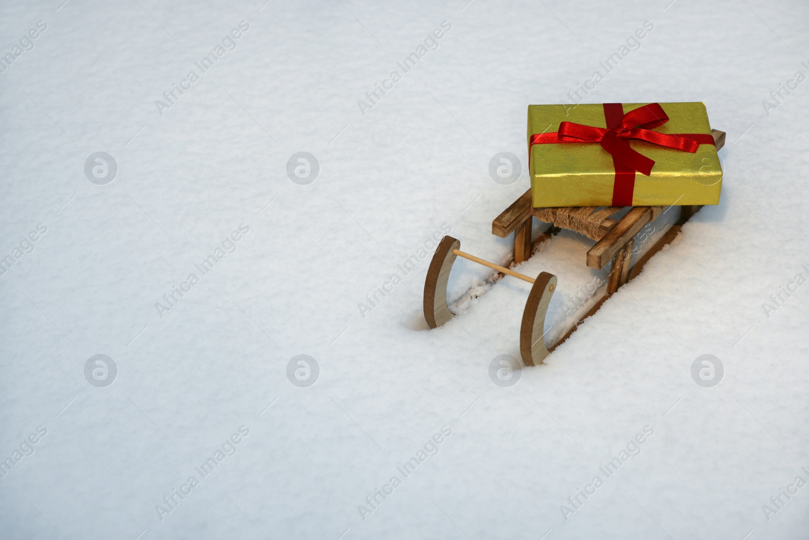 Photo of Wooden sleigh with gift box on snow outdoors. Space for text