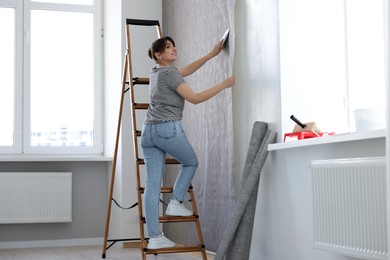 Photo of Woman smoothing stylish gray wallpaper in room