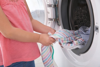 Adorable little girl taking clothes out of washing machine, closeup. Laundry day