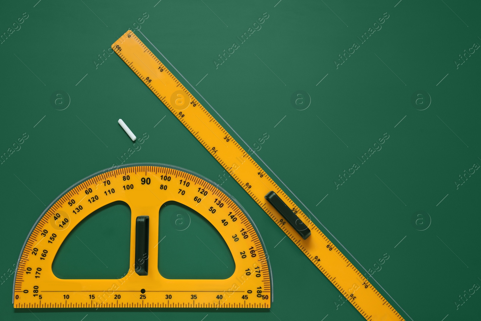 Photo of Protractor, ruler and chalk on green chalkboard, flat lay. Space for text