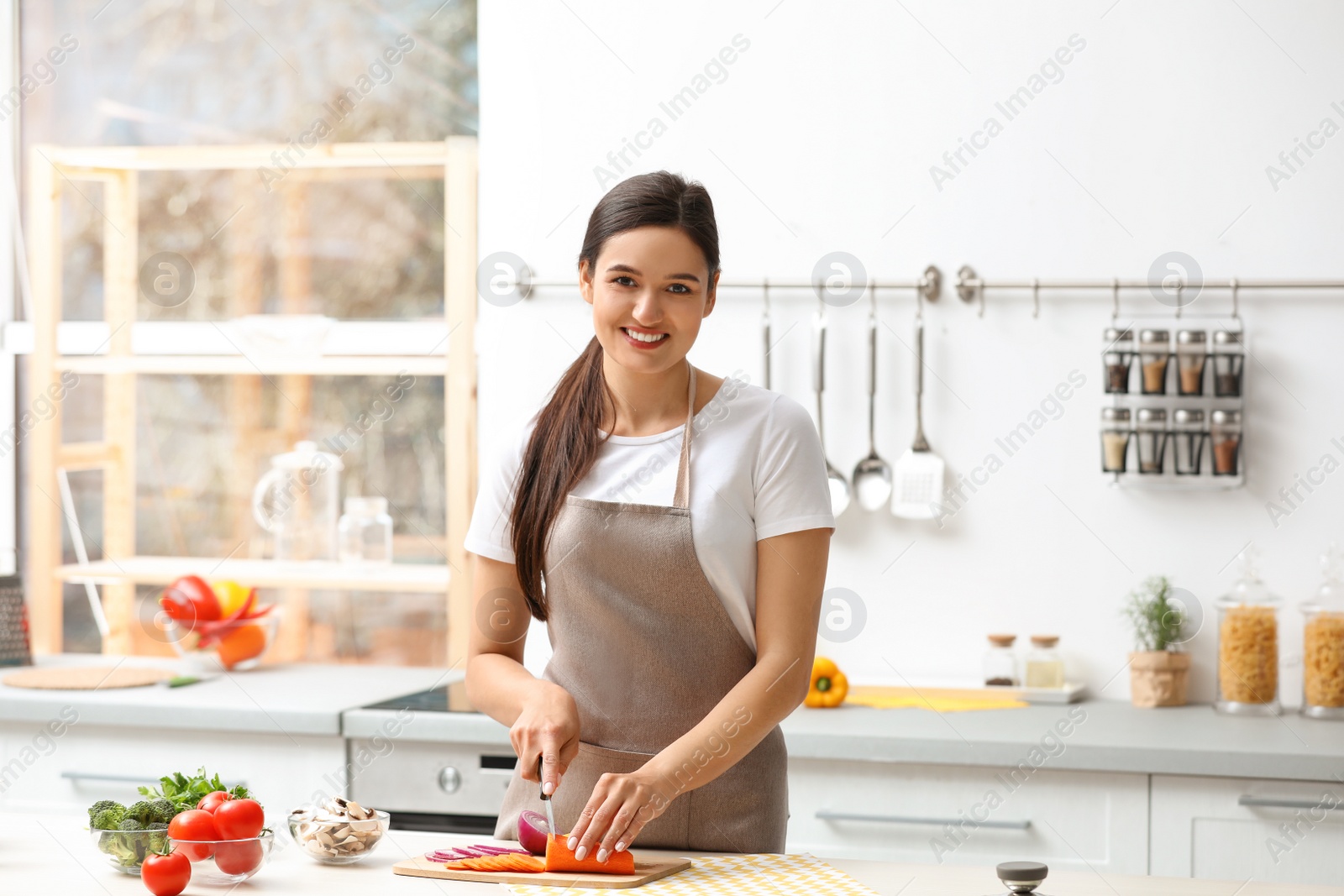 Photo of Young woman cutting vegetables for soup at table in kitchen