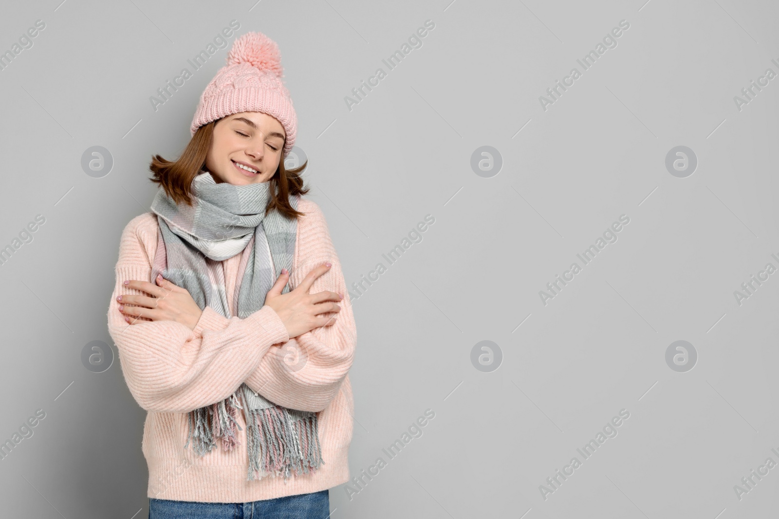 Photo of Beautiful woman in warm scarf and hat on gray background, space for text