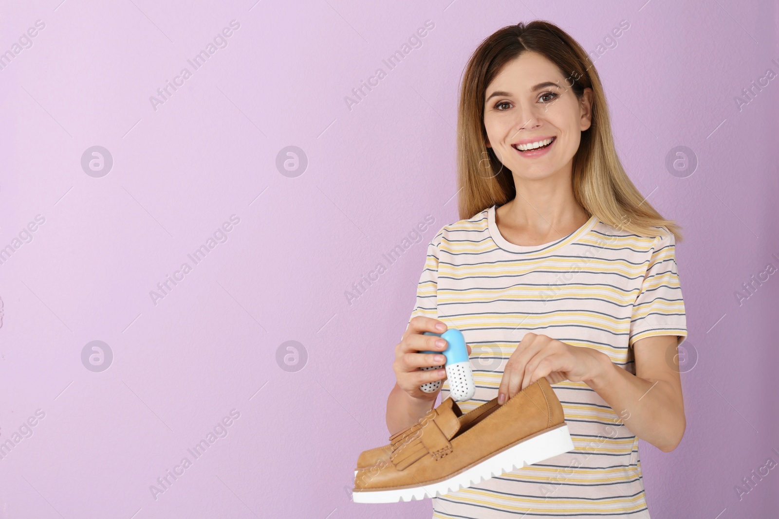 Photo of Woman putting capsule shoe freshener in footwear on color background