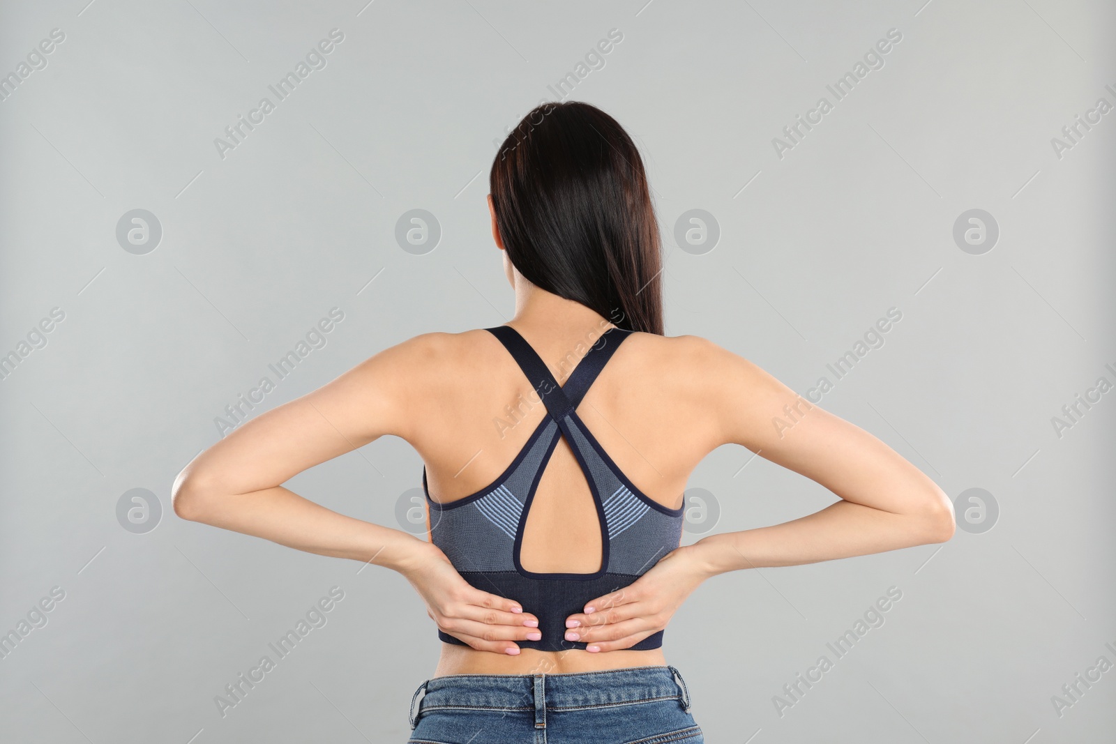 Photo of Woman suffering from lower back pain on light grey background. Visiting orthopedist