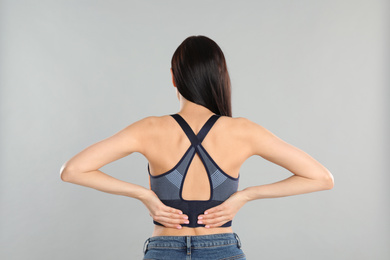 Woman suffering from lower back pain on light grey background. Visiting orthopedist