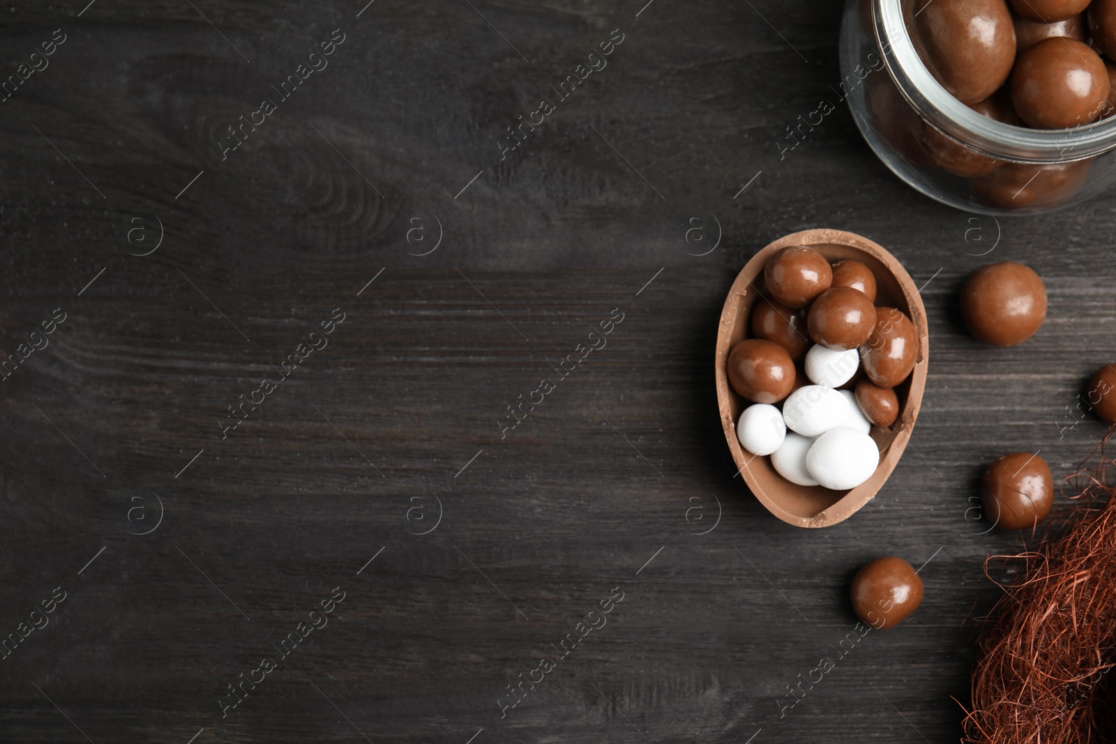 Photo of Half of tasty chocolate egg and candies on black wooden table, flat lay. Space for text