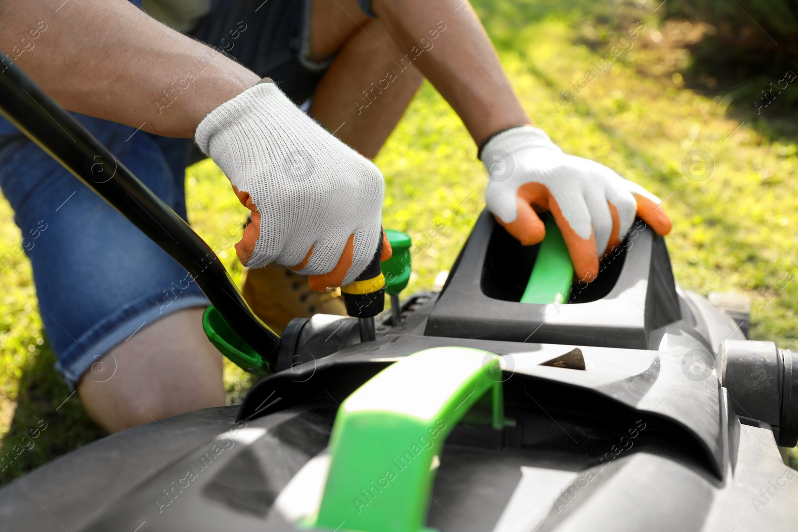 Photo of Young man with screwdriver fixing lawn mower in garden, closeup