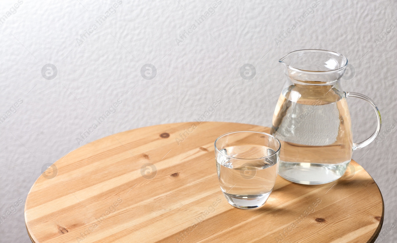 Photo of Pitcher and glass with water on table near white wall. Space for text