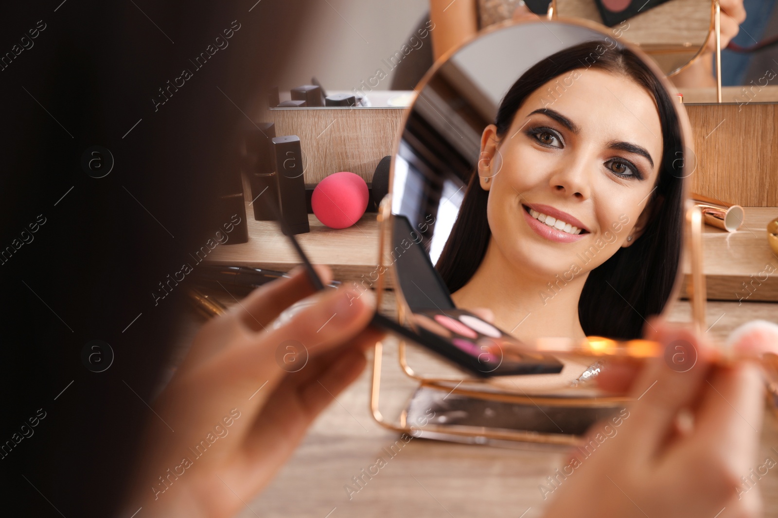 Photo of Beautiful young woman applying makeup near mirror at dressing table