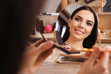 Beautiful young woman applying makeup near mirror at dressing table