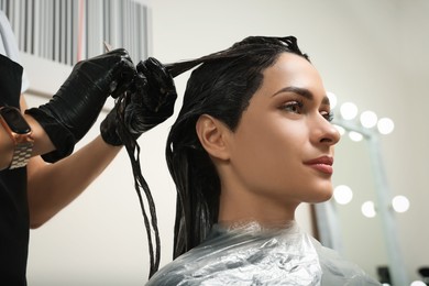 Photo of Professional hairdresser dyeing client's hair in beauty salon