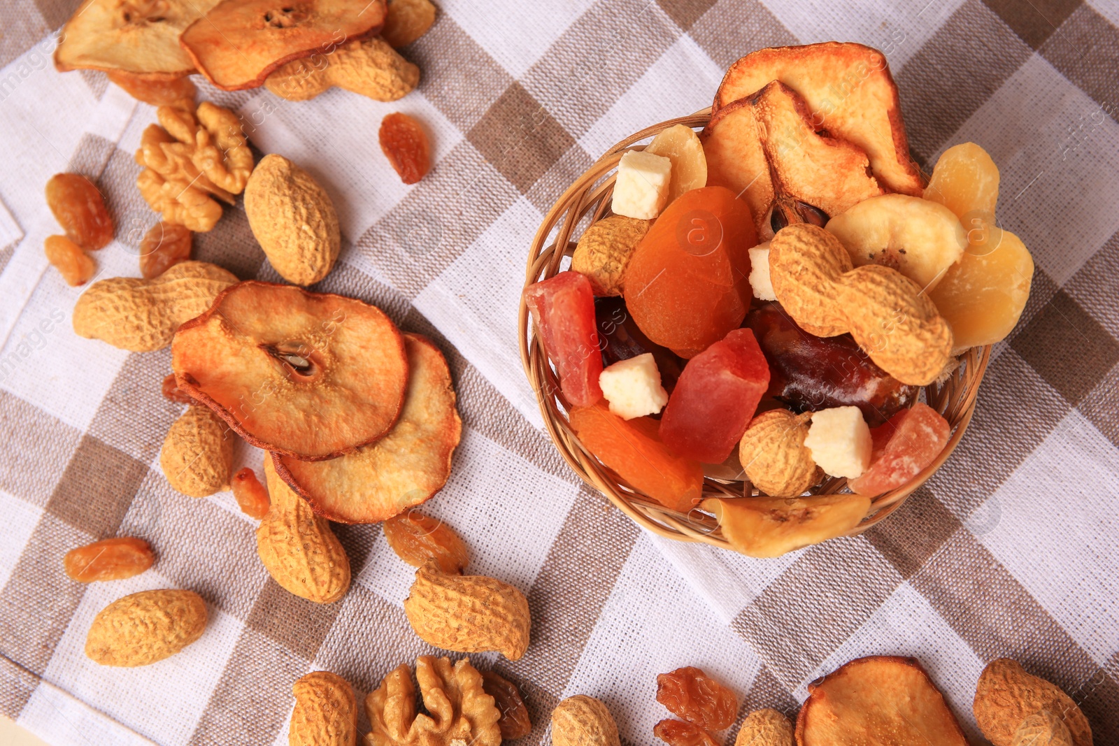 Photo of Mixed dried fruits and nuts on checkered tablecloth, flat lay