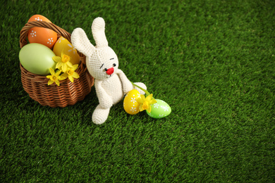 Photo of Colorful Easter eggs, rabbit and narcissus flowers on green grass. Space for text