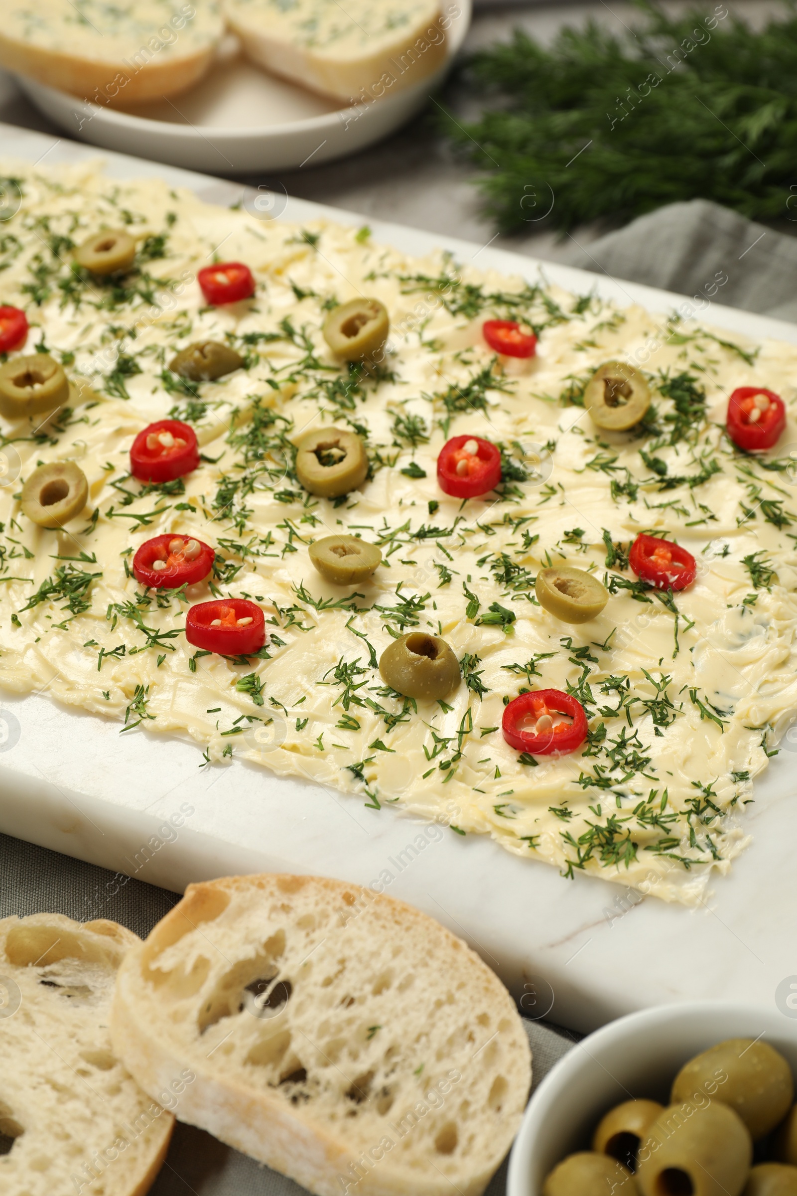 Photo of Fresh butter board with cut olives, pepper and bread on grey table, closeup