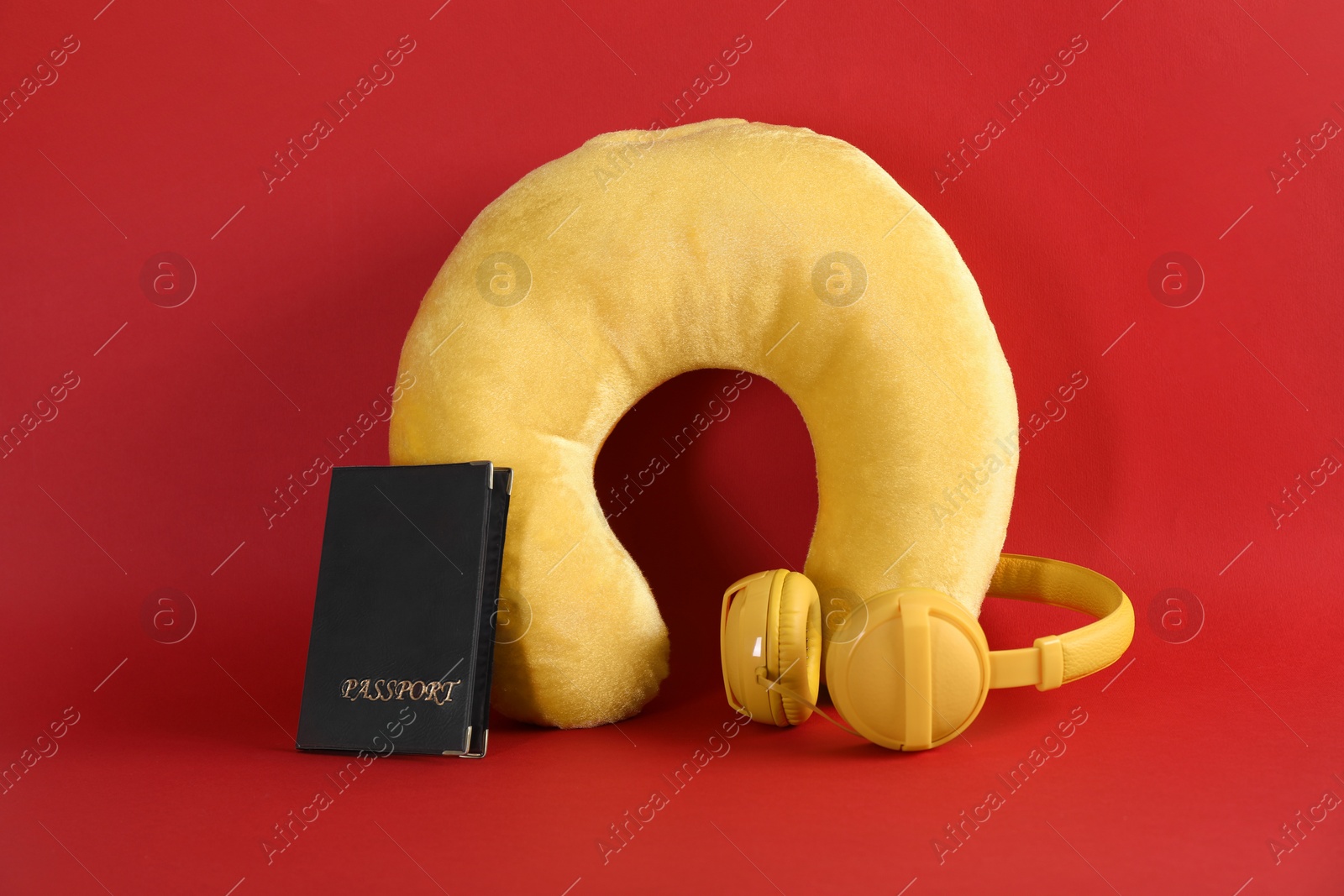 Photo of Yellow travel pillow, headphones and passport on red background