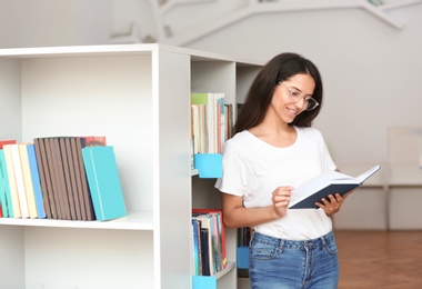 Photo of Young woman reading book near shelving unit in library