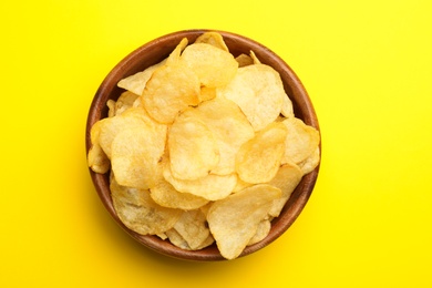 Delicious crispy potato chips in bowl on color background, top view