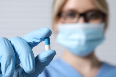 Photo of Doctor holding pill on light background, selective focus. Space for text