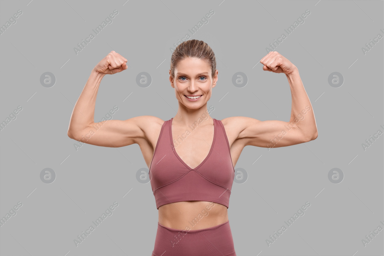 Photo of Portrait of sportswoman showing muscles on grey background