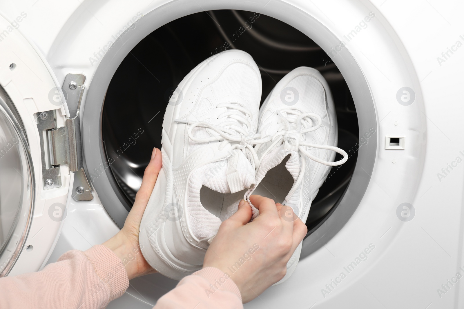 Photo of Woman putting stylish sneakers into washing machine, closeup