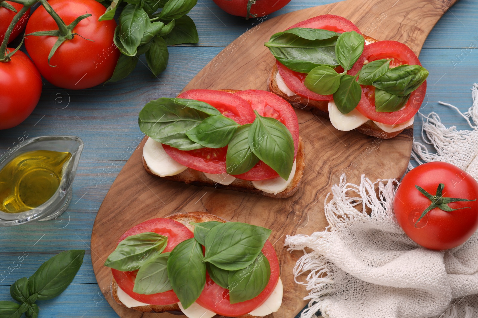 Photo of Delicious Caprese sandwiches with mozzarella, tomatoes and basil on light blue wooden table, flat lay