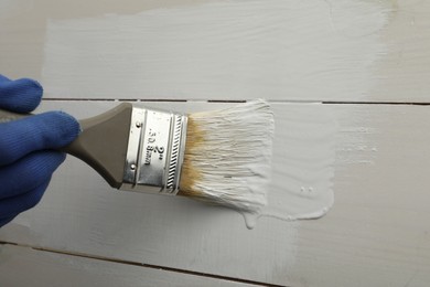 Worker applying white paint onto wooden surface, closeup. Space for text