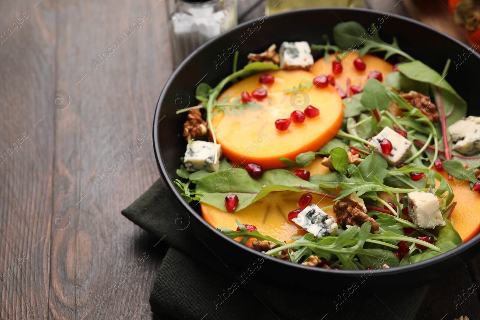 Photo of Tasty salad with persimmon, blue cheese, pomegranate and walnuts served on wooden table, closeup. Space for text