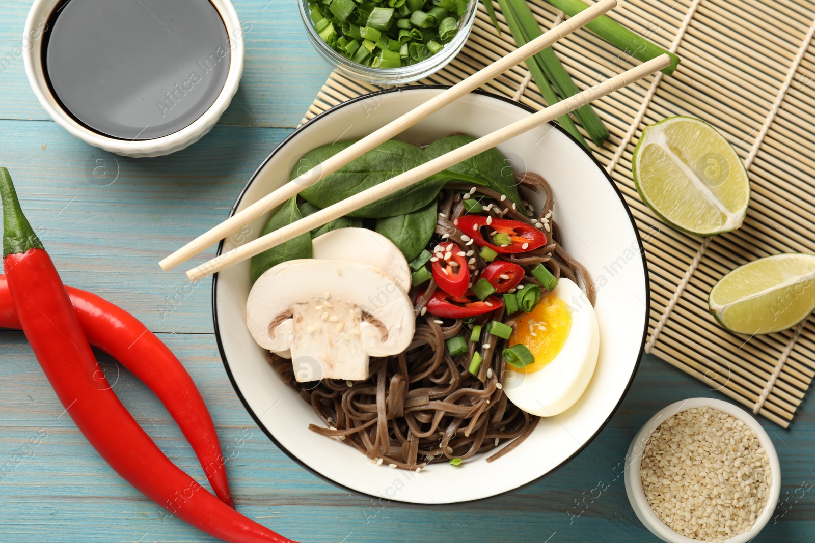 Photo of Flat lay composition with tasty buckwheat noodles (soba) and chopsticks on light blue wooden table