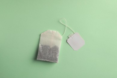 Photo of Paper tea bag with tag on light green background, top view