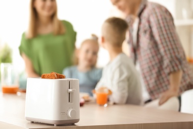 Photo of Preparing bread in toaster and blurred family on background