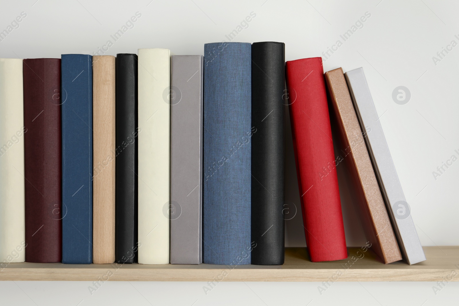 Photo of Wooden shelf with many hardcover books on white wall