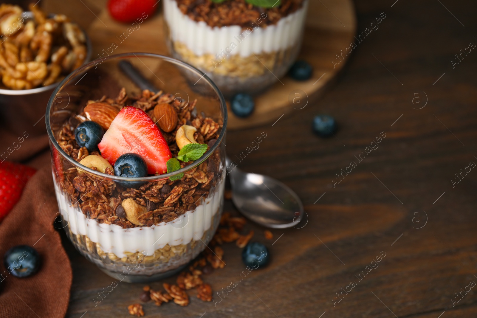 Photo of Tasty granola with berries, nuts, yogurt and chia seeds in glass on wooden table, closeup. Space for text