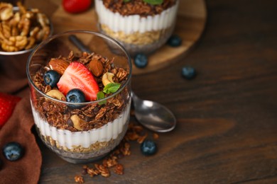 Photo of Tasty granola with berries, nuts, yogurt and chia seeds in glass on wooden table, closeup. Space for text