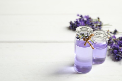 Photo of Bottles of essential oil and lavender flowers on white wooden table. Space for text