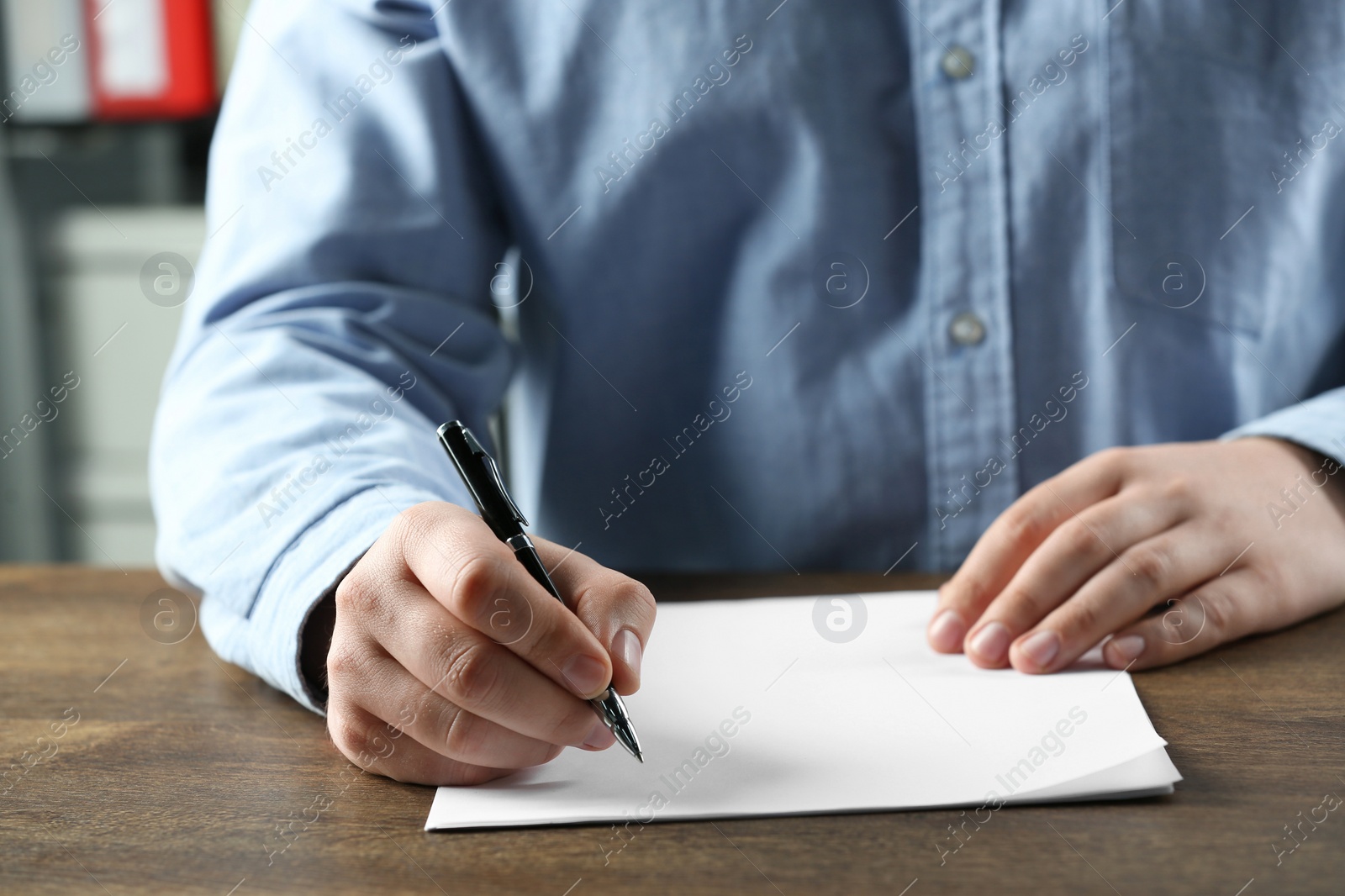 Photo of Man writing on sheet of paper with pen at wooden table, closeup