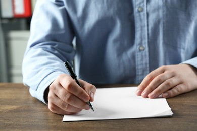 Photo of Man writing on sheet of paper with pen at wooden table, closeup