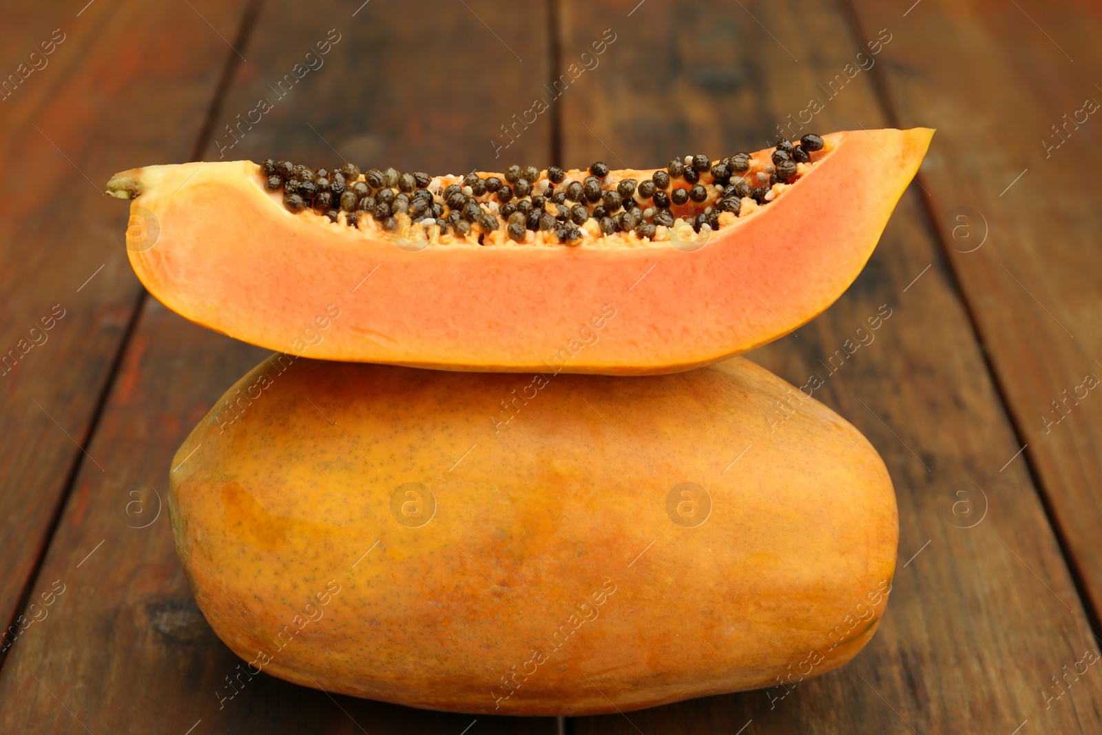 Photo of Tasty whole and half papaya fruits on wooden table, closeup