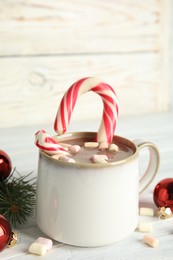Photo of Cup of tasty cocoa with marshmallows, candy cane and Christmas decor on white wooden table
