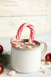 Cup of tasty cocoa with marshmallows, candy cane and Christmas decor on white wooden table