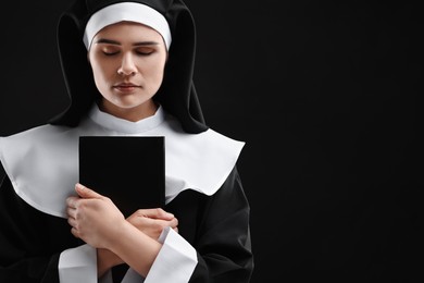 Photo of Nun with Bible on black background, space for text