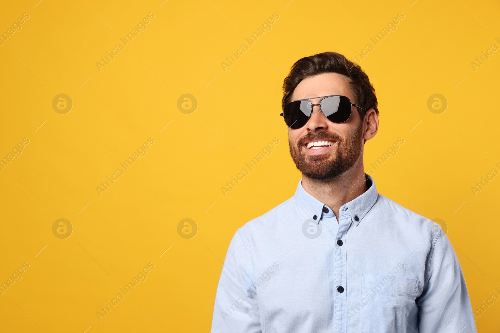 Photo of Portrait of smiling bearded man with stylish sunglasses on orange background. Space for text