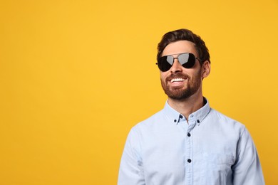 Photo of Portrait of smiling bearded man with stylish sunglasses on orange background. Space for text