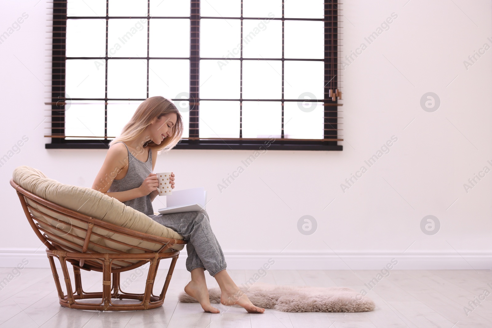 Photo of Young woman reading book near window with blinds at home. Space for text