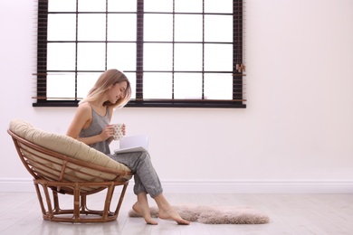 Photo of Young woman reading book near window with blinds at home. Space for text