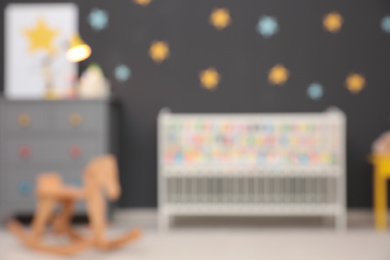 Photo of Blurred view of cute baby room interior with modern crib and rocking horse