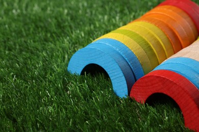 Photo of Colorful wooden pieces of play set on green grass, closeup with space for text. Educational toy for motor skills development