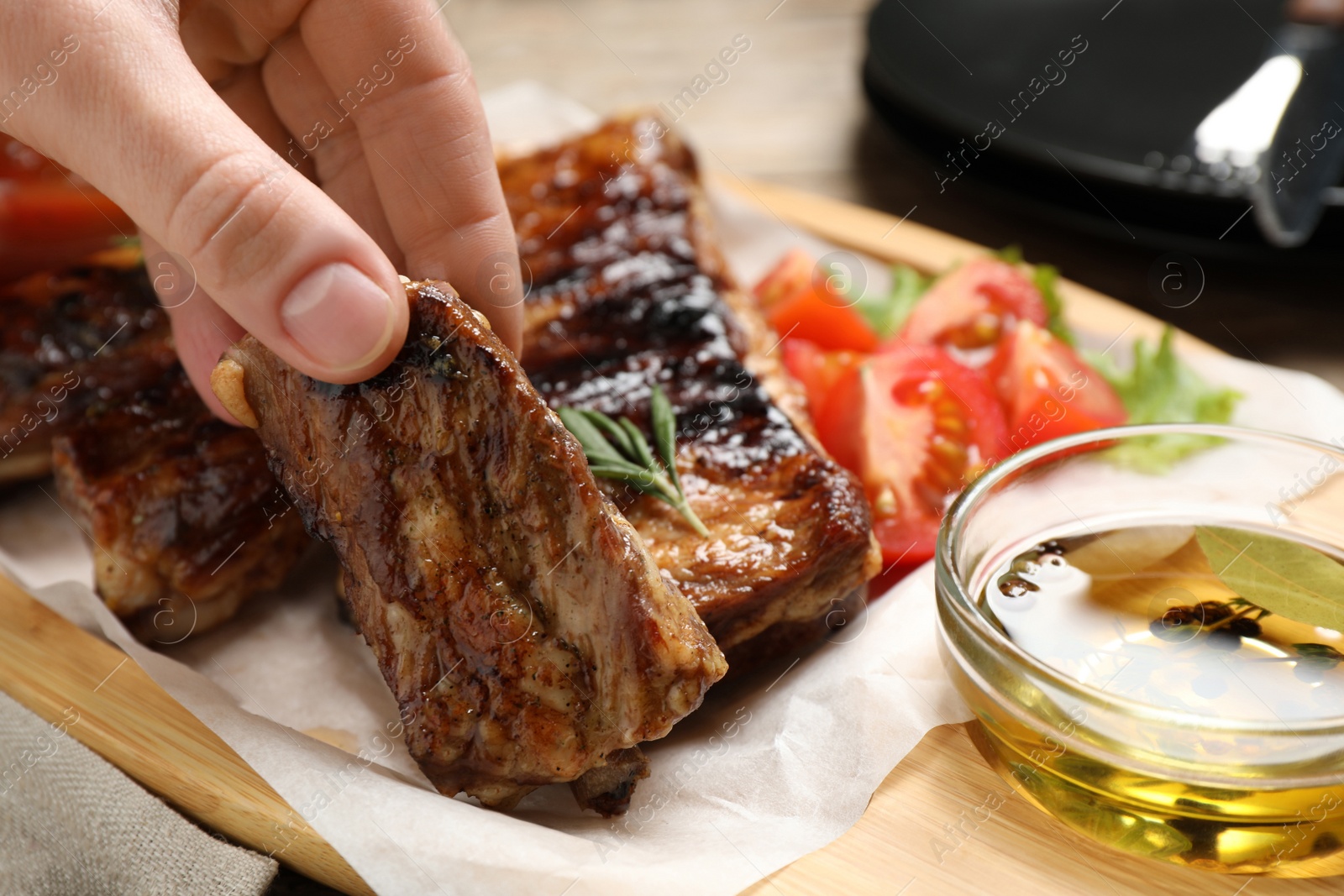 Photo of Woman with tasty grilled ribs at table, closeup